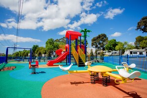 A playground with a red slide, yellow and blue play structures, and a swing set. - BIG4 Melbourne Holiday Park (Coburg North)