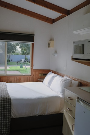 Un dormitorio con cama, mesita de noche, microondas y ventana.