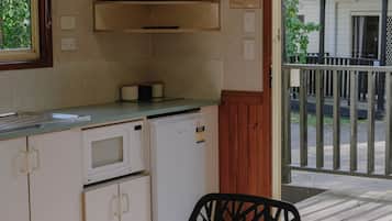 A kitchen with a flat-screen TV, a microwave, and a refrigerator. There is a glass table with a chair in front.