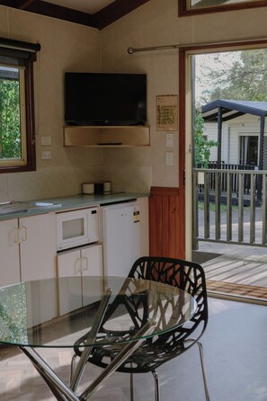 A kitchen with a flat-screen TV, a microwave, and a refrigerator. There is a glass table with a chair in front. - BIG4 Melbourne Holiday Park (Coburg North)