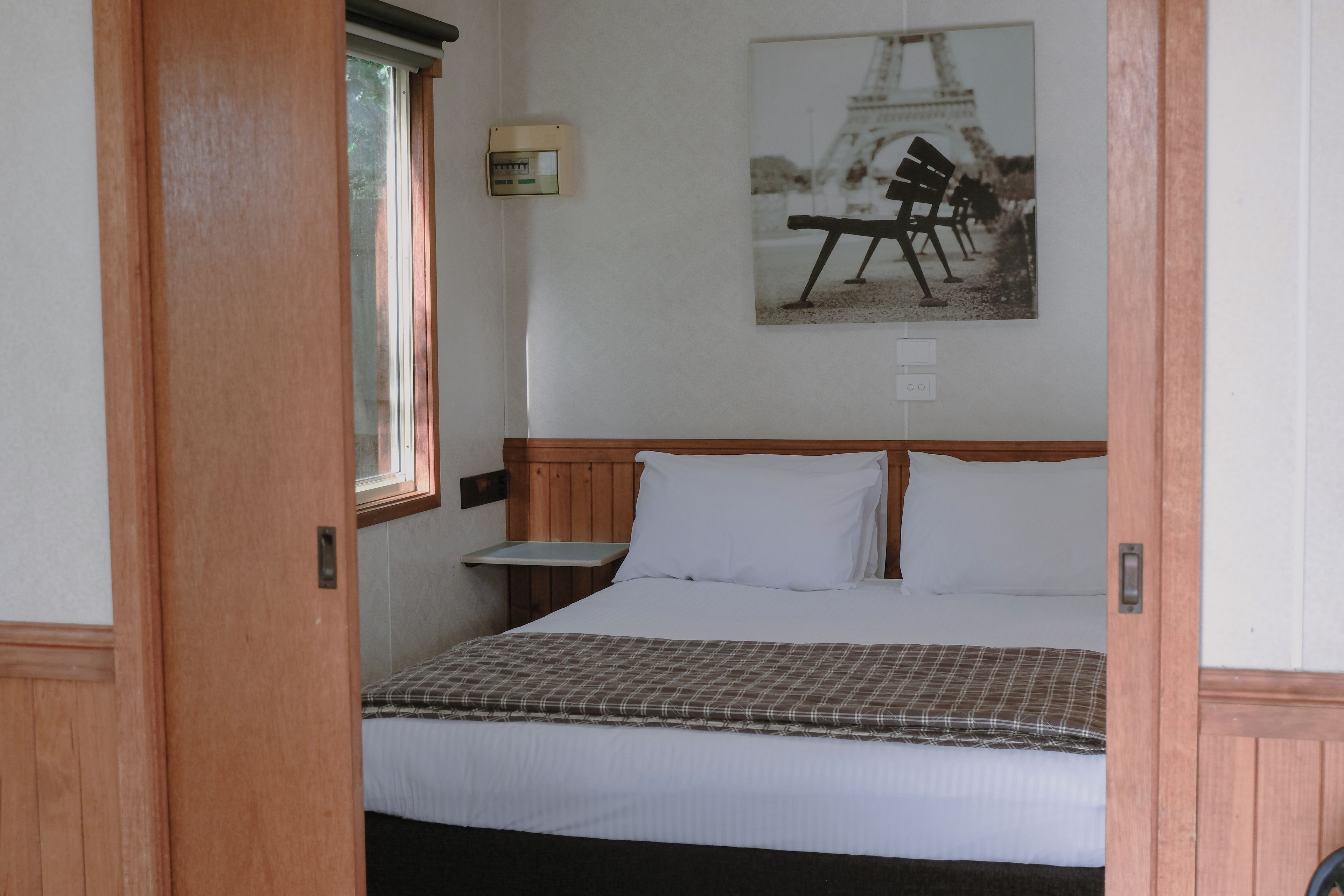 A bedroom with a bed, a nightstand, a wall-mounted lamp, and a picture of a crane.