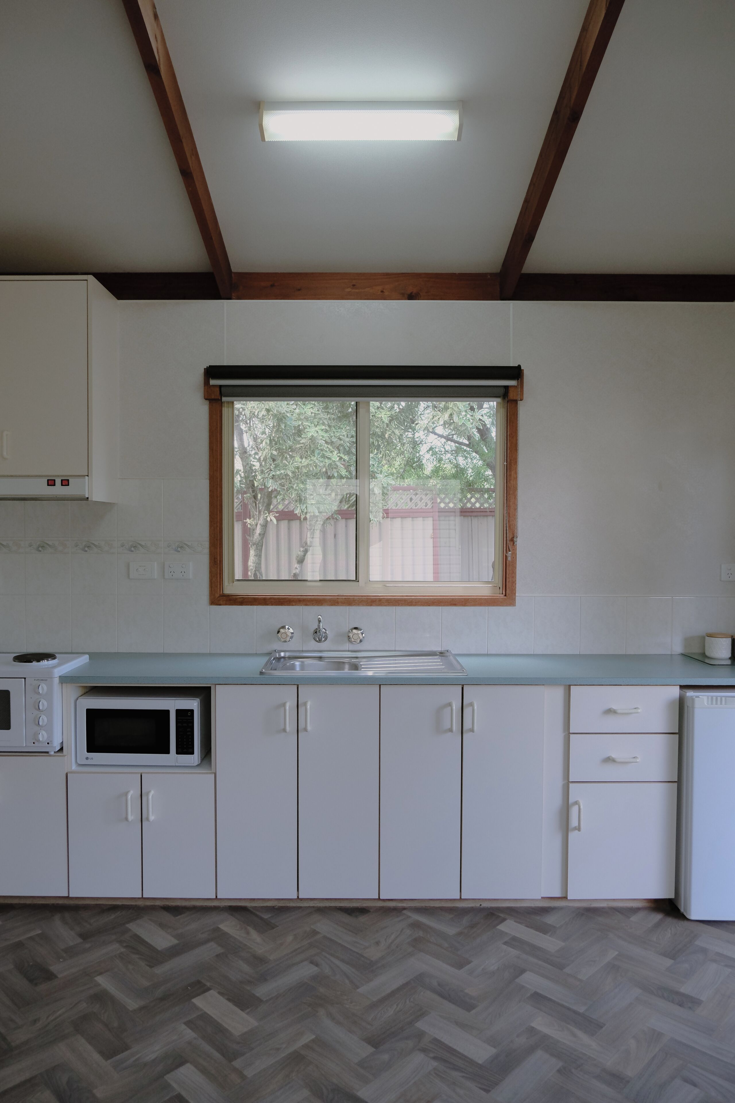 A kitchen with white cabinets, a microwave, a stove, and a window with a view of trees.