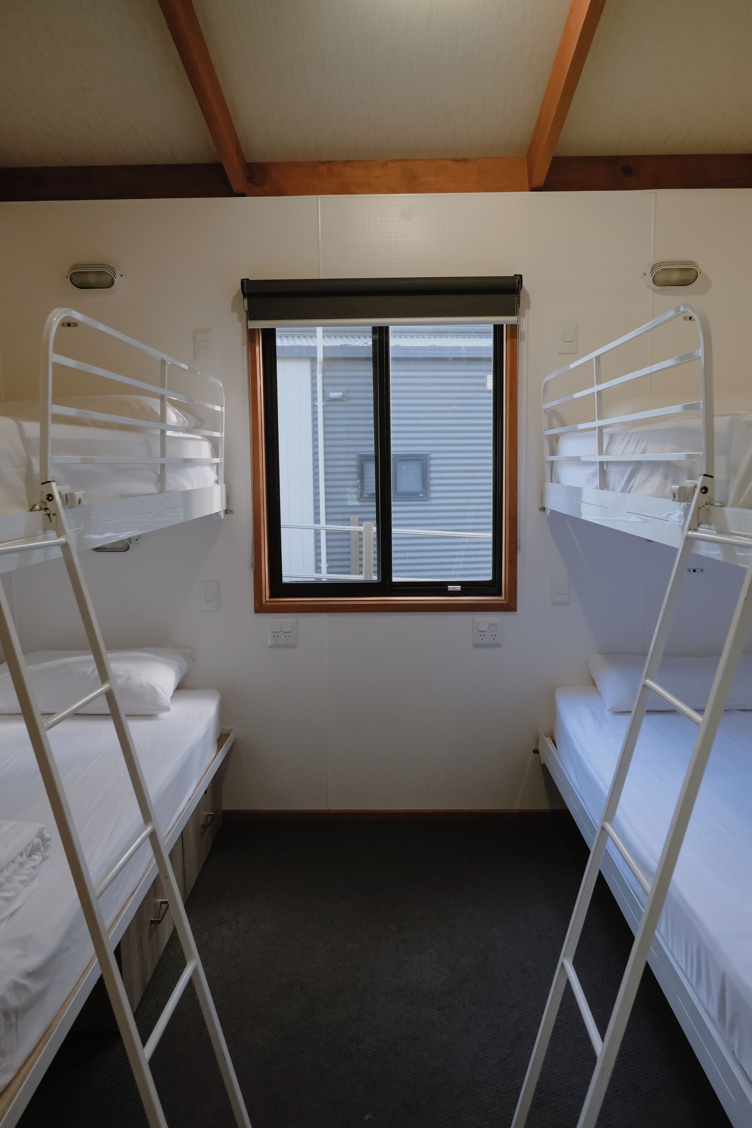 A room with bunk beds, a window with blinds, and a ceiling vent.