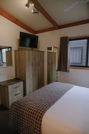 A bedroom with a bed, a wardrobe, a television, and a window with curtains. - BIG4 Melbourne Holiday Park (Coburg North)