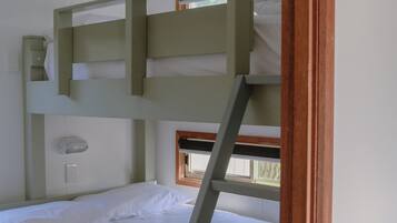 A bunk bed with a ladder, white bedding, a small window, and wooden beams.