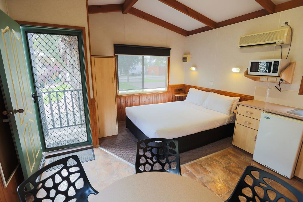 A small, cozy room with a bed, a desk, a chair, and a microwave.