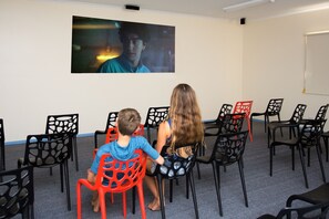 A room with rows of black and red chairs facing a wall-mounted screen displaying a movie scene. - BIG4 Melbourne Holiday Park (Coburg North)