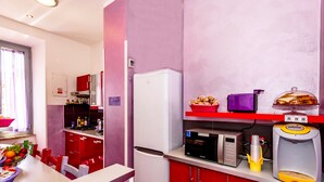 A kitchen with a refrigerator, microwave, and a water dispenser. There are red cabinets and a window with curtains. - Dream Station (Rome)