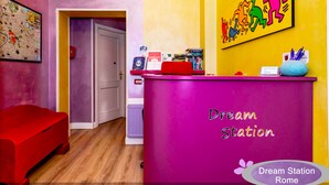 A brightly colored reception area with a purple counter labeled "Dream Station Rome," a red bench, and a wall with a colorful illustration. - Dream Station (Rome)