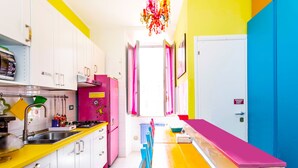 A brightly colored kitchen with white cabinets, a pink refrigerator, and a yellow countertop. - Dream Station (Rome)