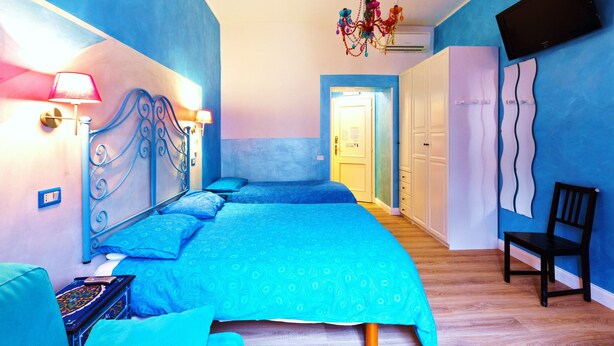 A bedroom with a blue theme, featuring a bed with a headboard, a chair, and a chandelier. - Dream Station (Rome)