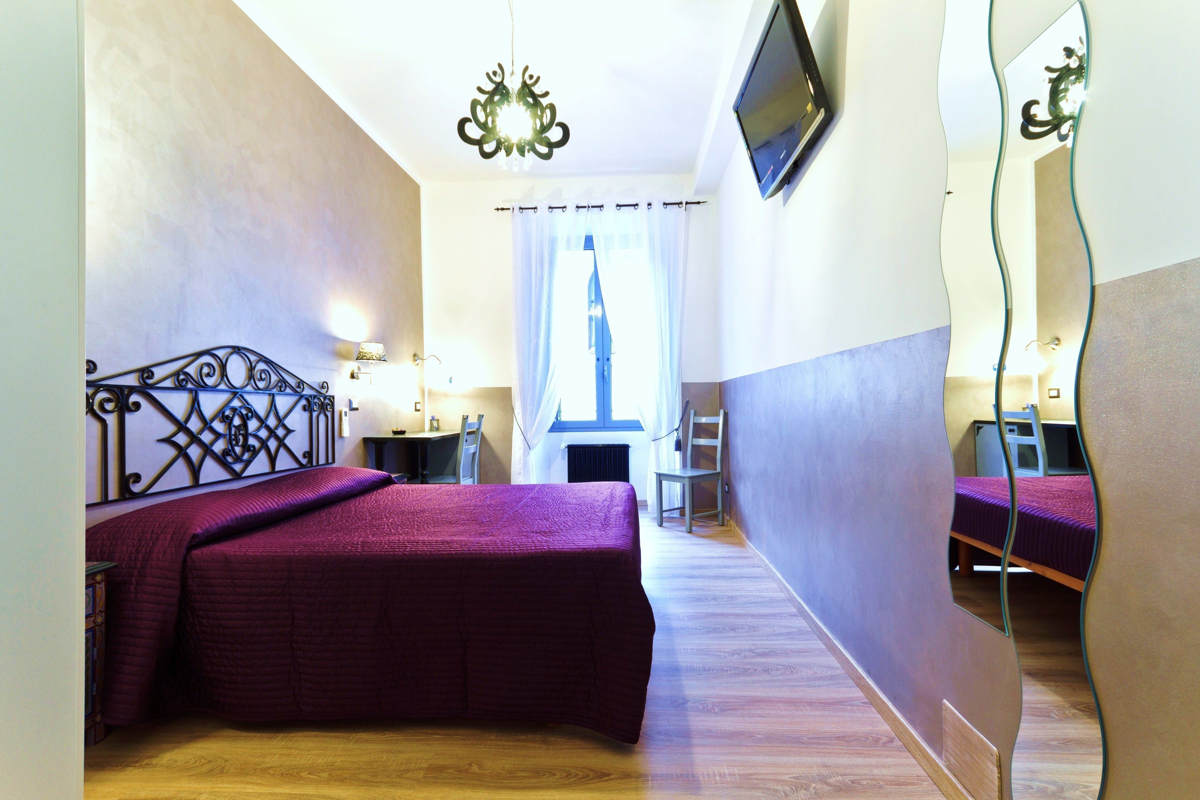 A bedroom with a bed, a desk, a chair, a TV, and a window with curtains.
