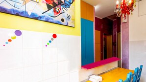 A modern dining area with a colorful abstract painting, a vibrant chandelier, and a bright yellow table. - Dream Station (Rome)