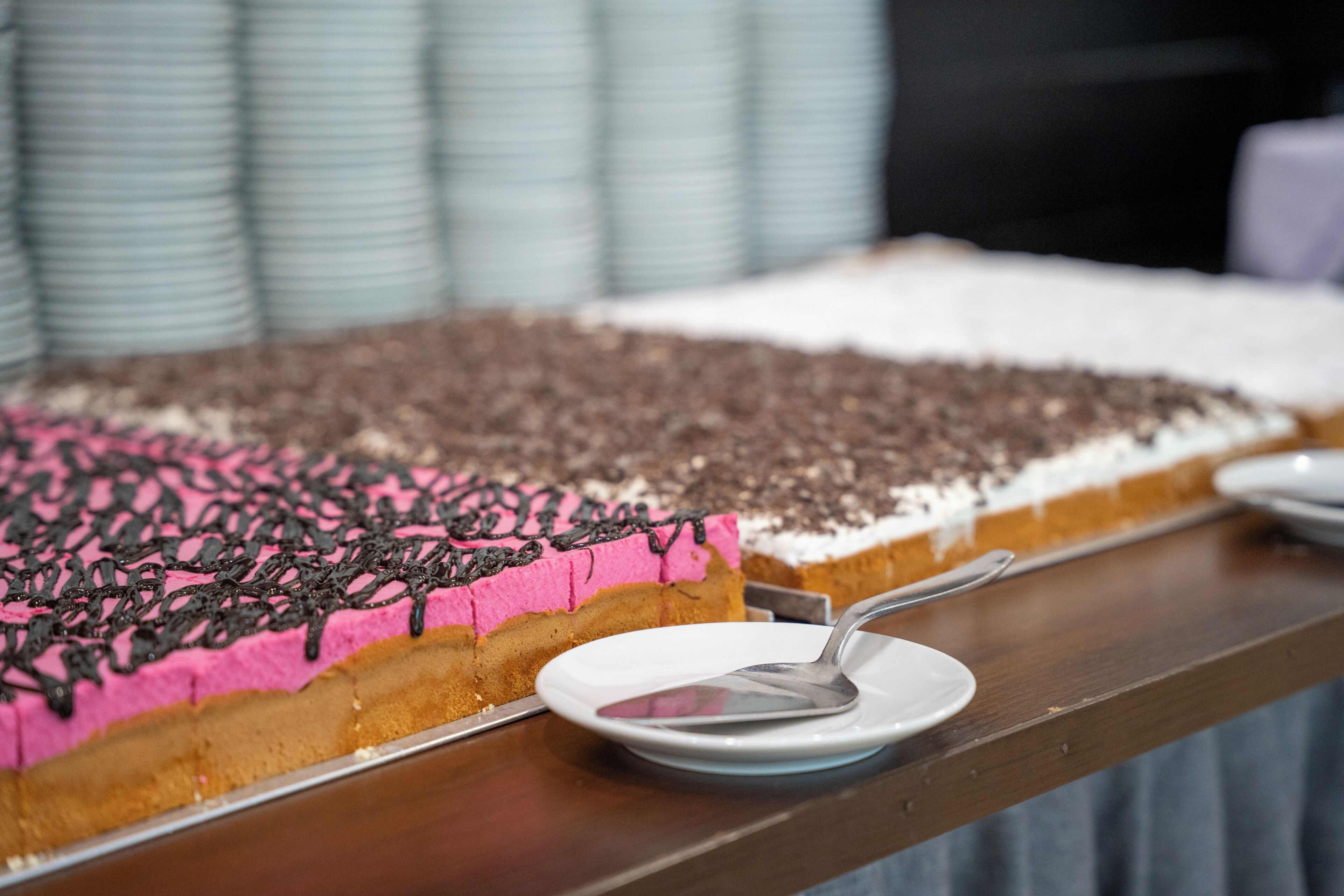 A dessert tray with a pink and white cake, a spoon, and plates on a wooden table.