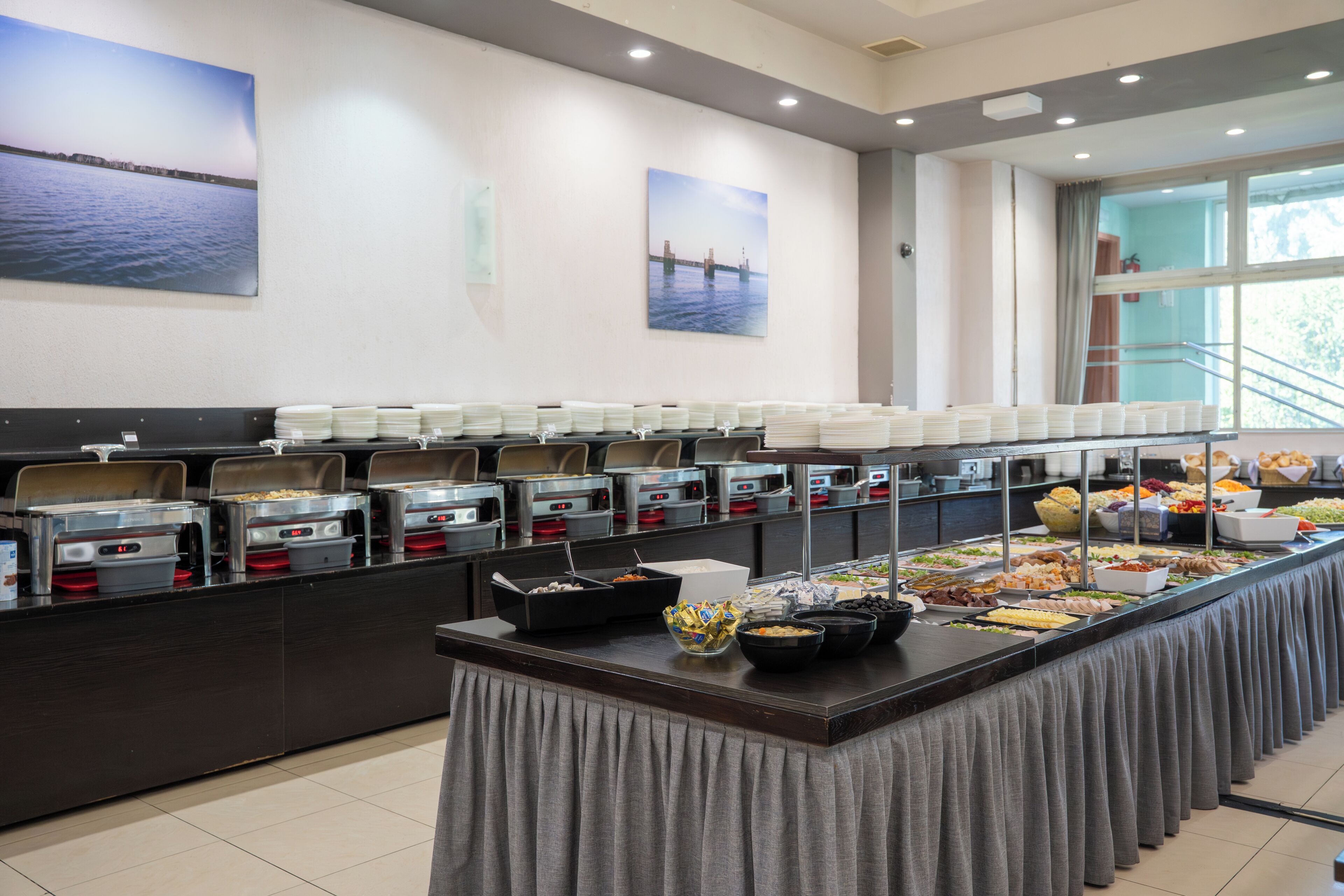 A buffet setup with various food containers and a view of the sea through the window.