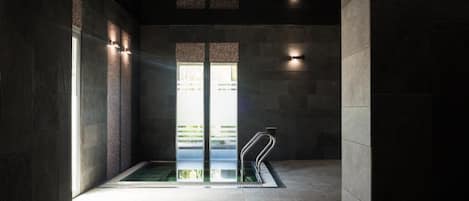 Ein Wellnessbereich mit einem gläsernen Whirlpool, Steinwänden und indirekter Beleuchtung.