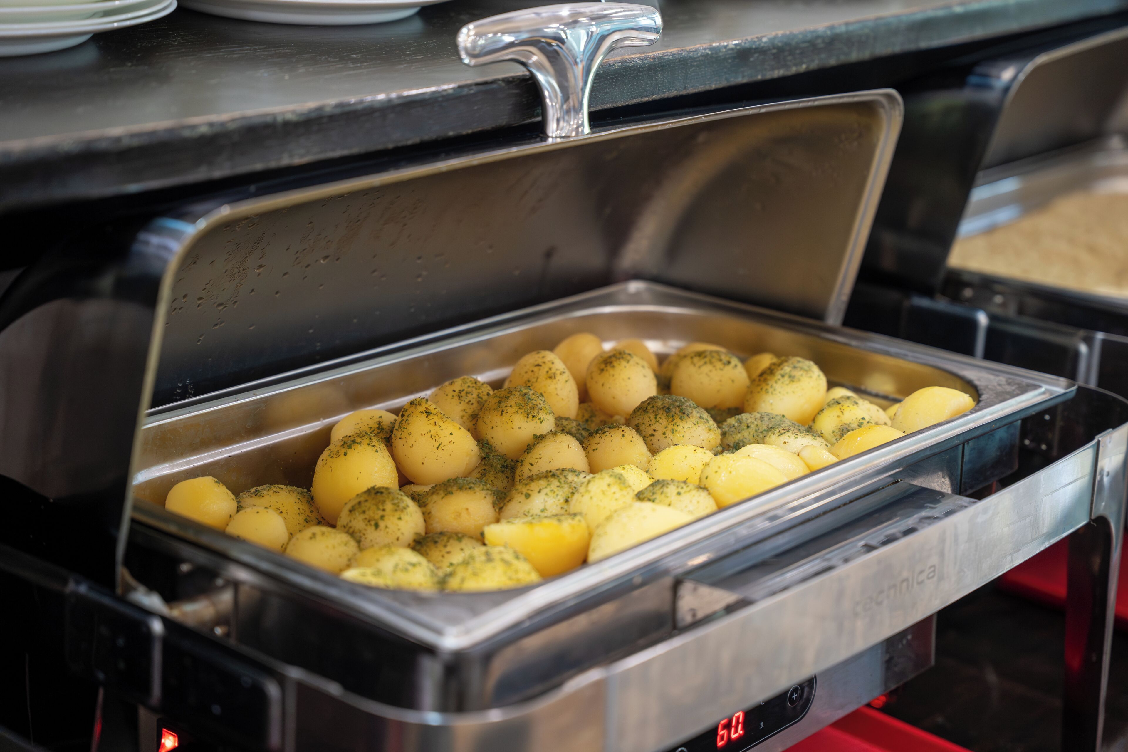 A buffet with a stainless steel serving tray containing potatoes.