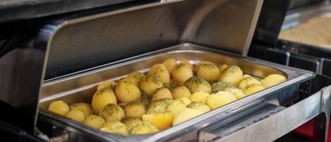 A buffet with a stainless steel serving tray containing potatoes.