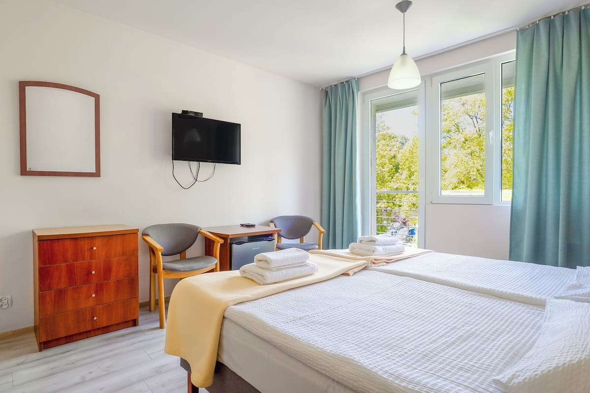 Hotellihuone, jossa on sänky, työpöytä, tuoli, televisio ja ikkuna, jossa on verhot.