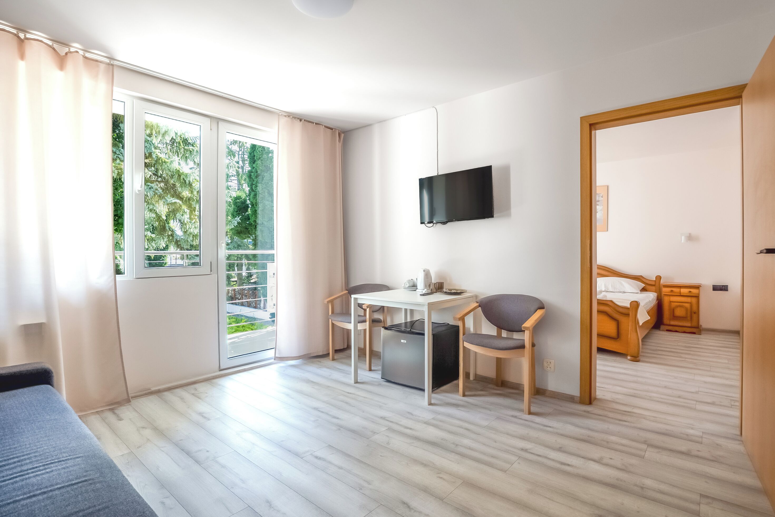 A room with a bed, a TV mounted on the wall, a table with chairs, and a sliding glass door leading to an outdoor area.