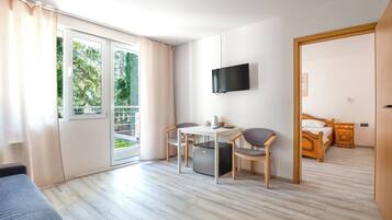 Une pièce comprenant un lit, un téléviseur fixé au mur, une table avec des chaises et une porte-fenêtre coulissante donnant sur un espace extérieur.