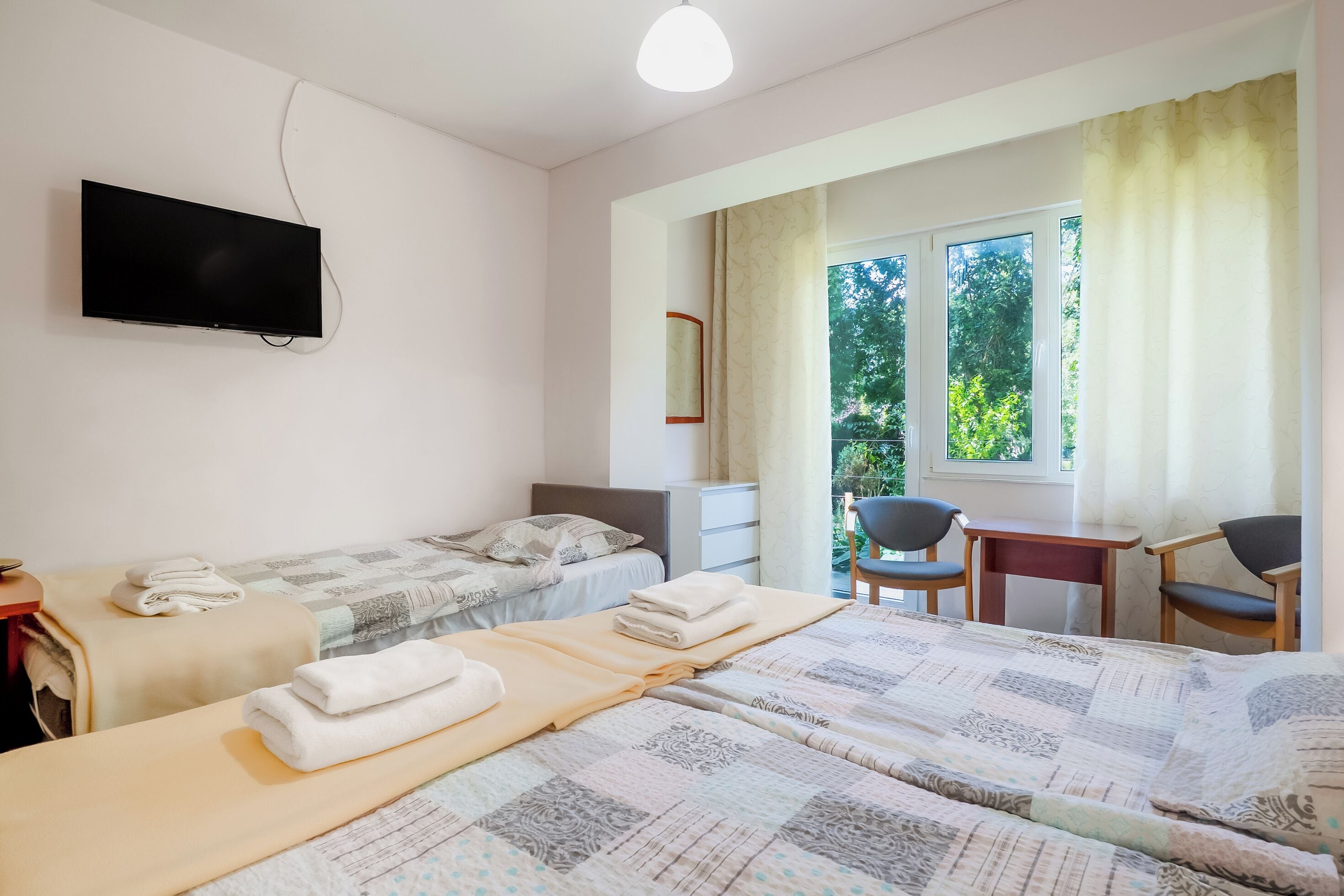 Camera d'albergo con due letti, una scrivania, sedie, una televisione e una finestra con tende.