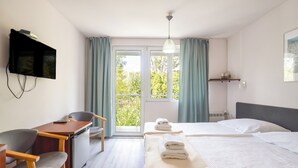 A hotel room with a bed, a desk with a chair, a television mounted on the wall, and a window with curtains. - Graal Spa (Swinoujscie)