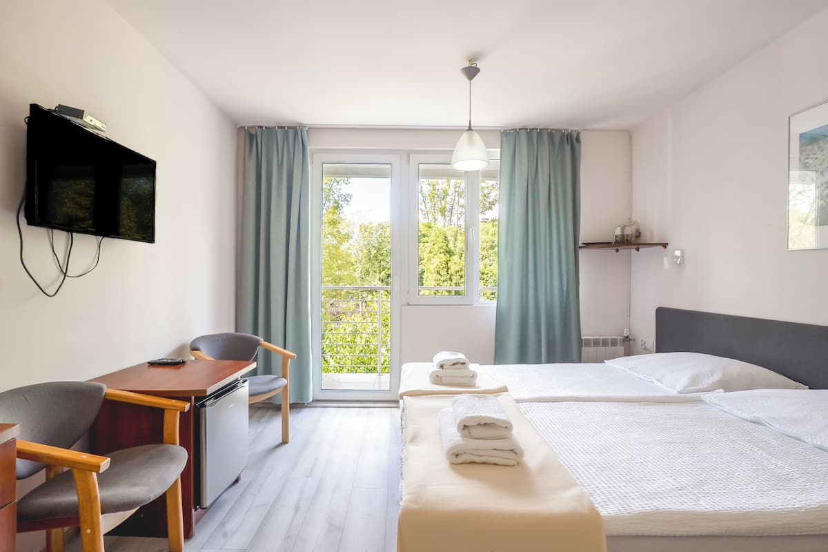 Hotellihuone, jossa on sänky, työpöytä tuolilla, seinälle asennettu televisio ja ikkuna, jossa on verhot.