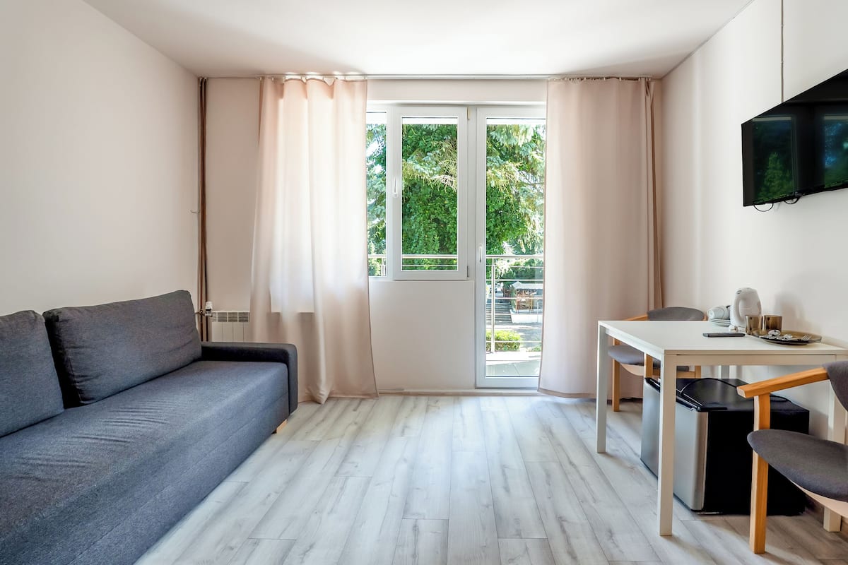 Moderni olohuone, jossa on sohva, ruokapöytä tuoleineen, seinälle asennettu televisio ja liukuovi, joka johtaa parvekkeelle.