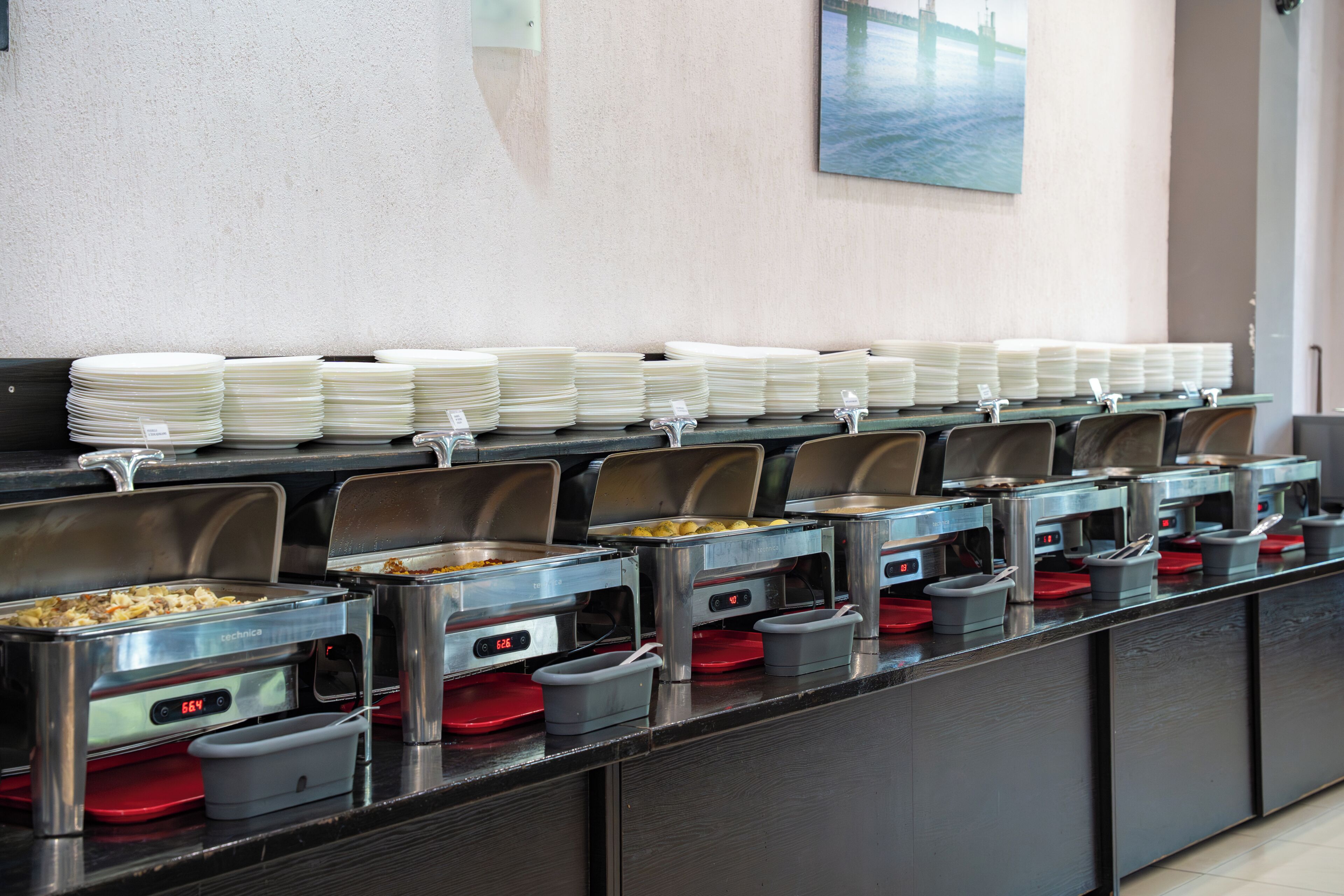 Montaje de bufé con varias estaciones de servicio, cada una con una bandeja de comida y una pila de platos blancos.