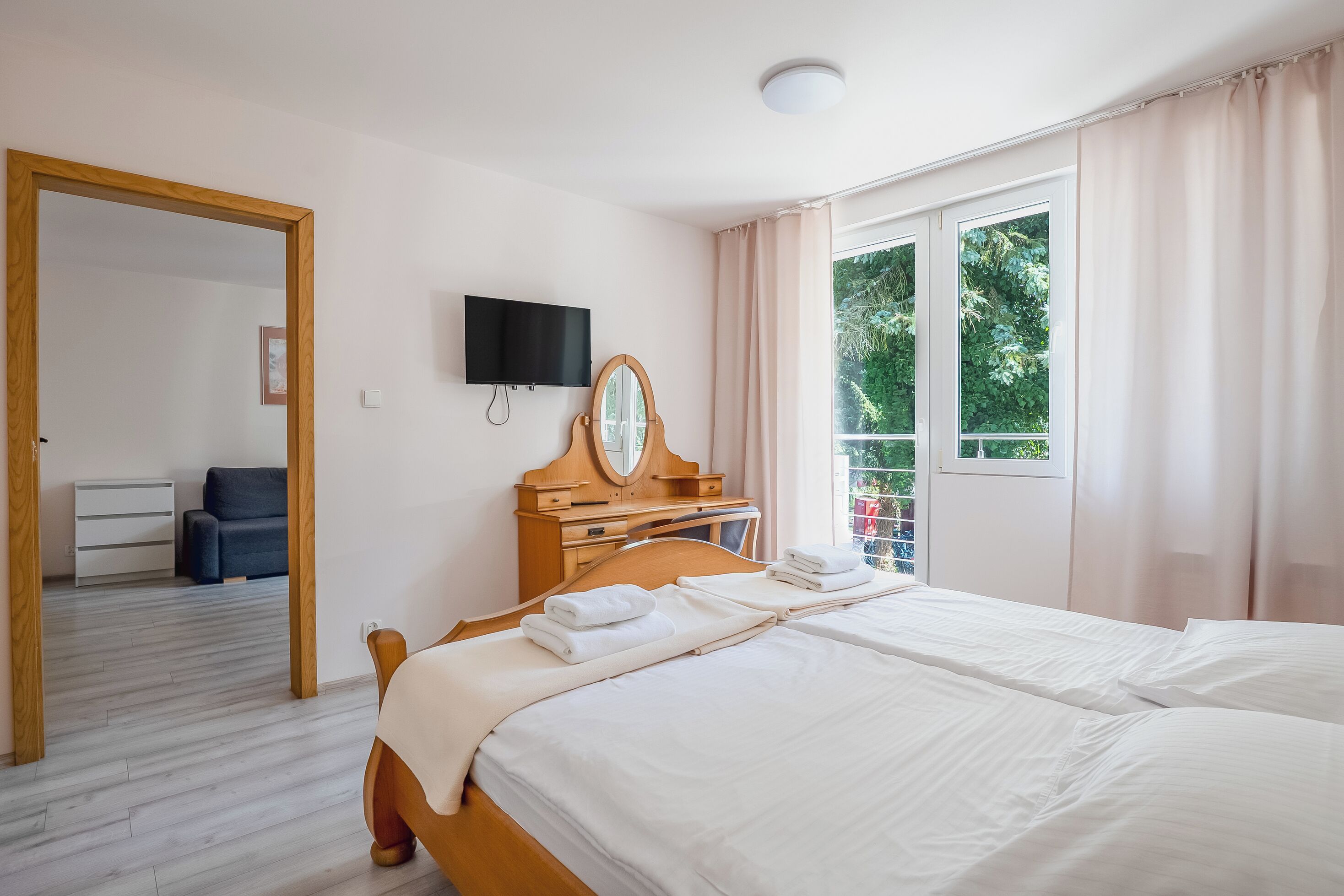 A hotel room with a bed, a TV, a wooden dresser, a mirror, and a window with curtains.