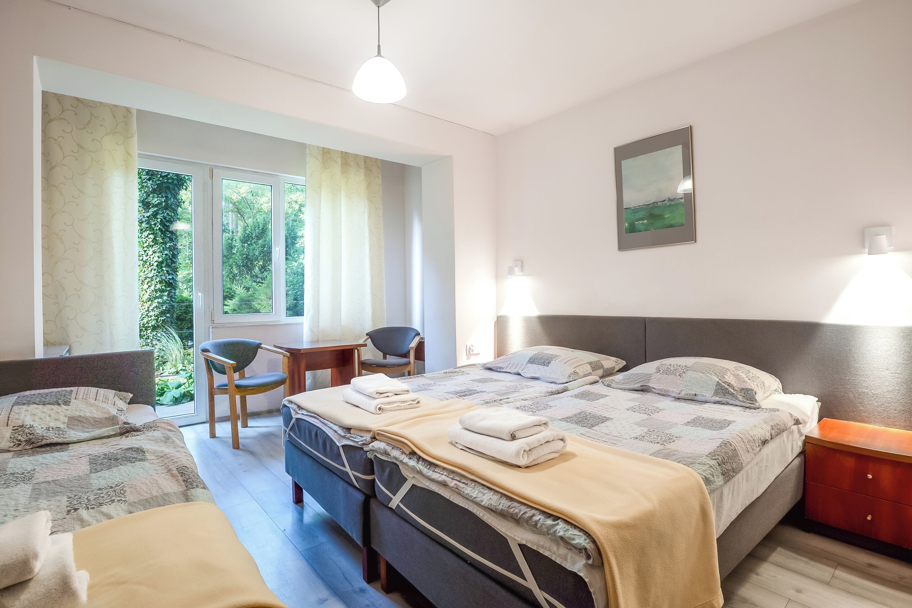 Un dormitorio con dos camas, una silla, un escritorio y una ventana con vistas al verdor.