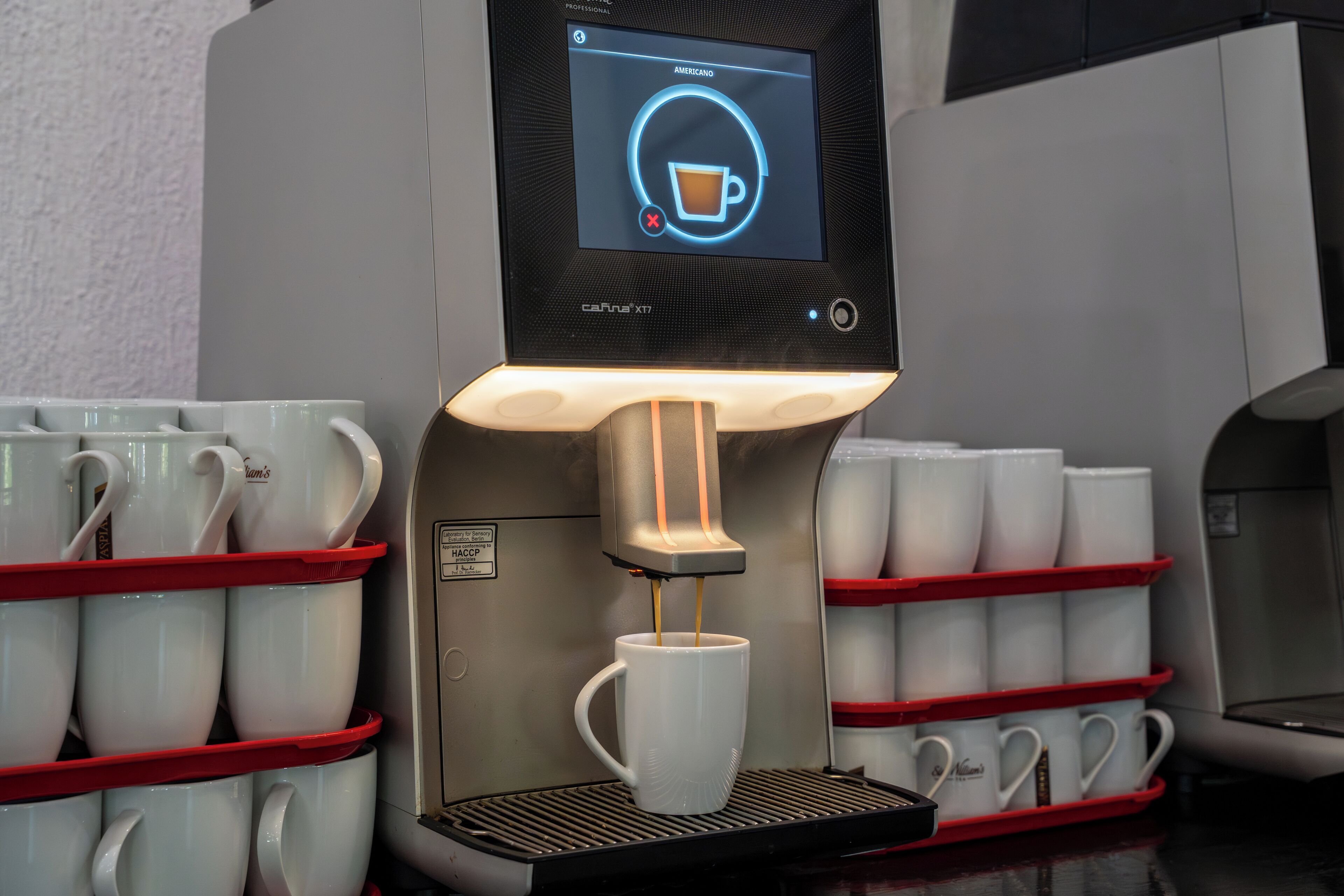 A coffee machine with a digital display, multiple coffee cups, and a coffee pod holder.