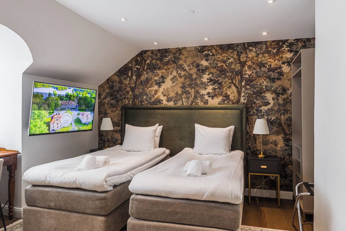 Una habitación de hotel con dos camas, un televisor en la pared y un papel tapiz con estampado floral.