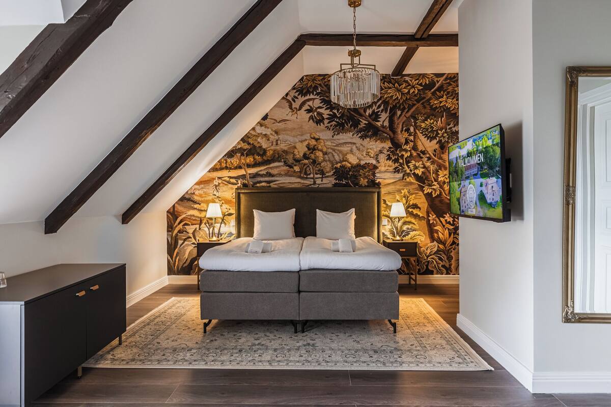 Un dormitorio con cama, candelabro, televisor y un mural.