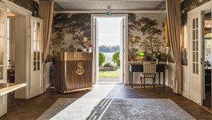 Een kamer met een houten receptiebalie, een kamerbreed tapijt en uitzicht op een tuin door een open deur.