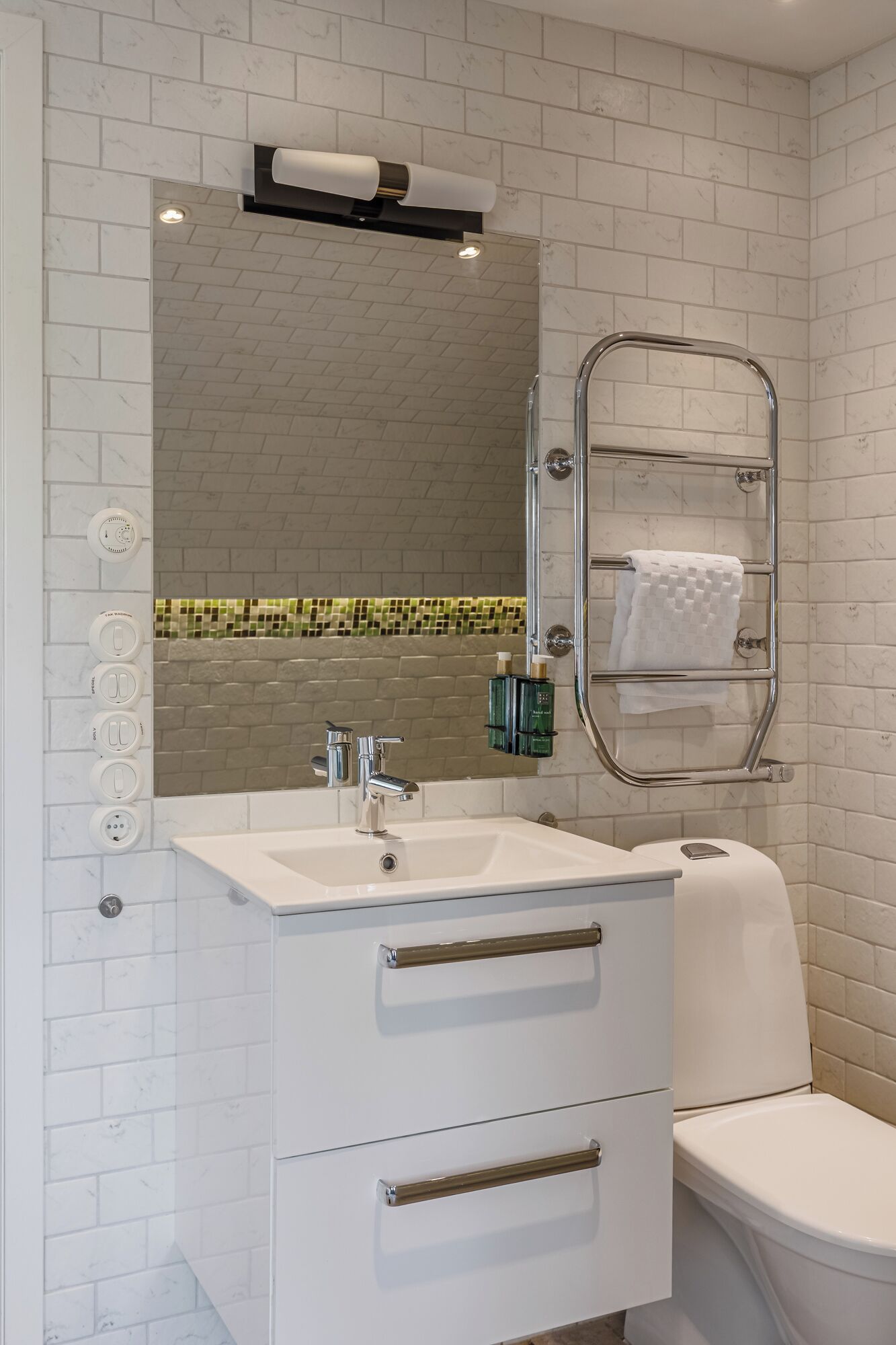 Un baño con lavamanos blanco, espejo y perchero.