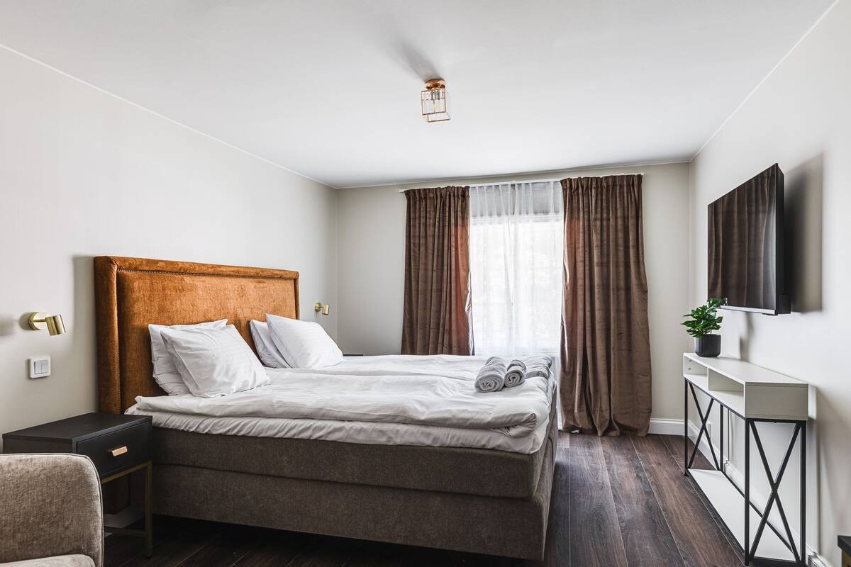 Un dormitorio moderno con una cama grande, una mesita de noche, un escritorio, una silla y un televisor montado en la pared.