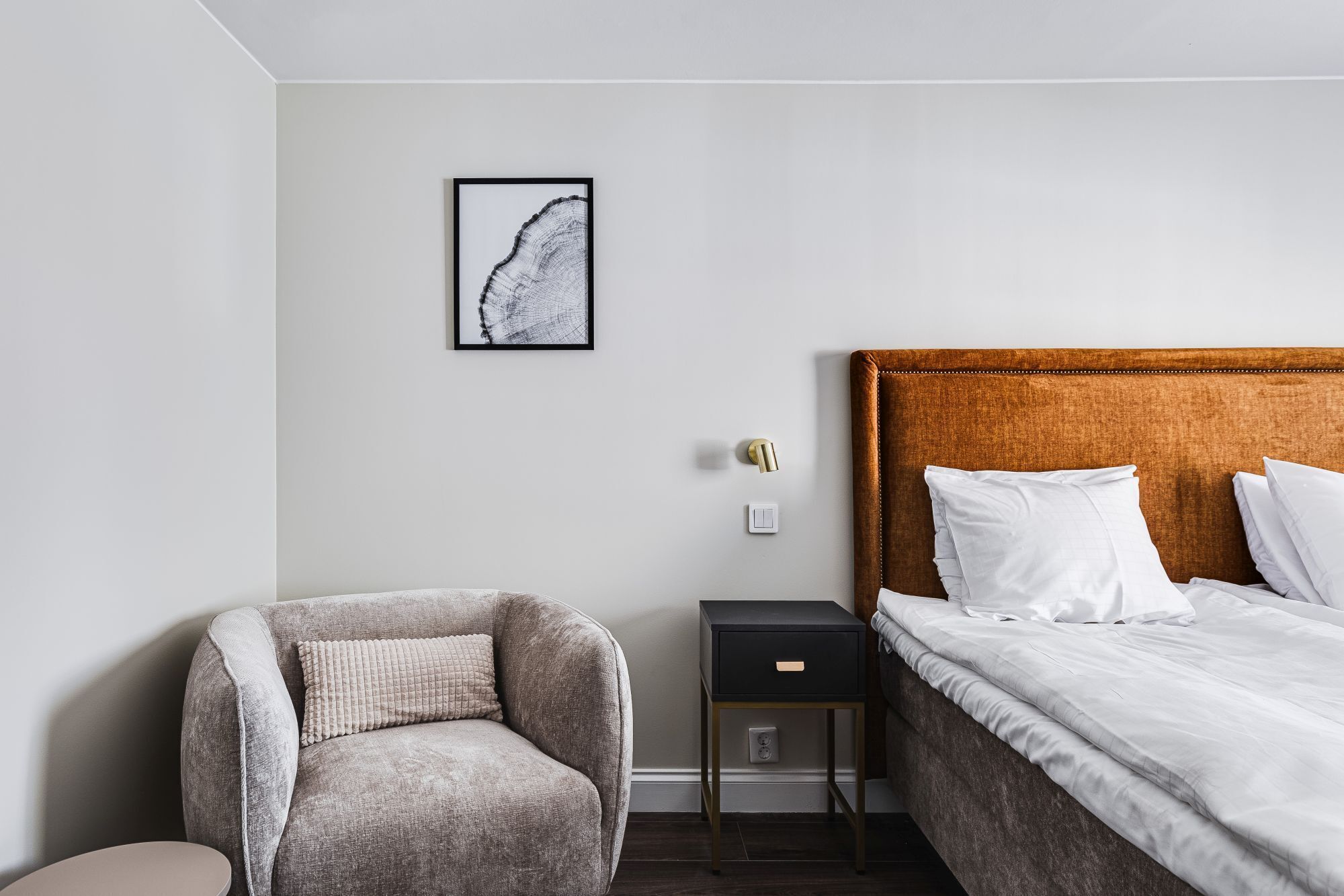 Une chambre à coucher comprenant un lit, une chaise, une table de chevet et un interrupteur fixé au mur.