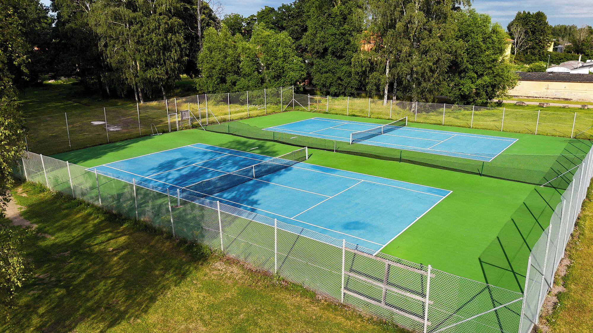 Ein Tennisplatzkomplex mit mehreren Plätzen, umgeben von einem Maschendrahtzaun und Bäumen im Hintergrund.