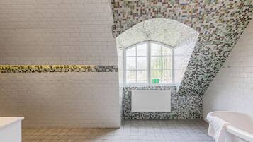 A bathroom with a tiled floor, a window, and a bathtub.