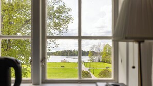 Een kamer met een groot raam, met uitzicht op een meer, een gazon en een gebouw aan de overkant van het water.