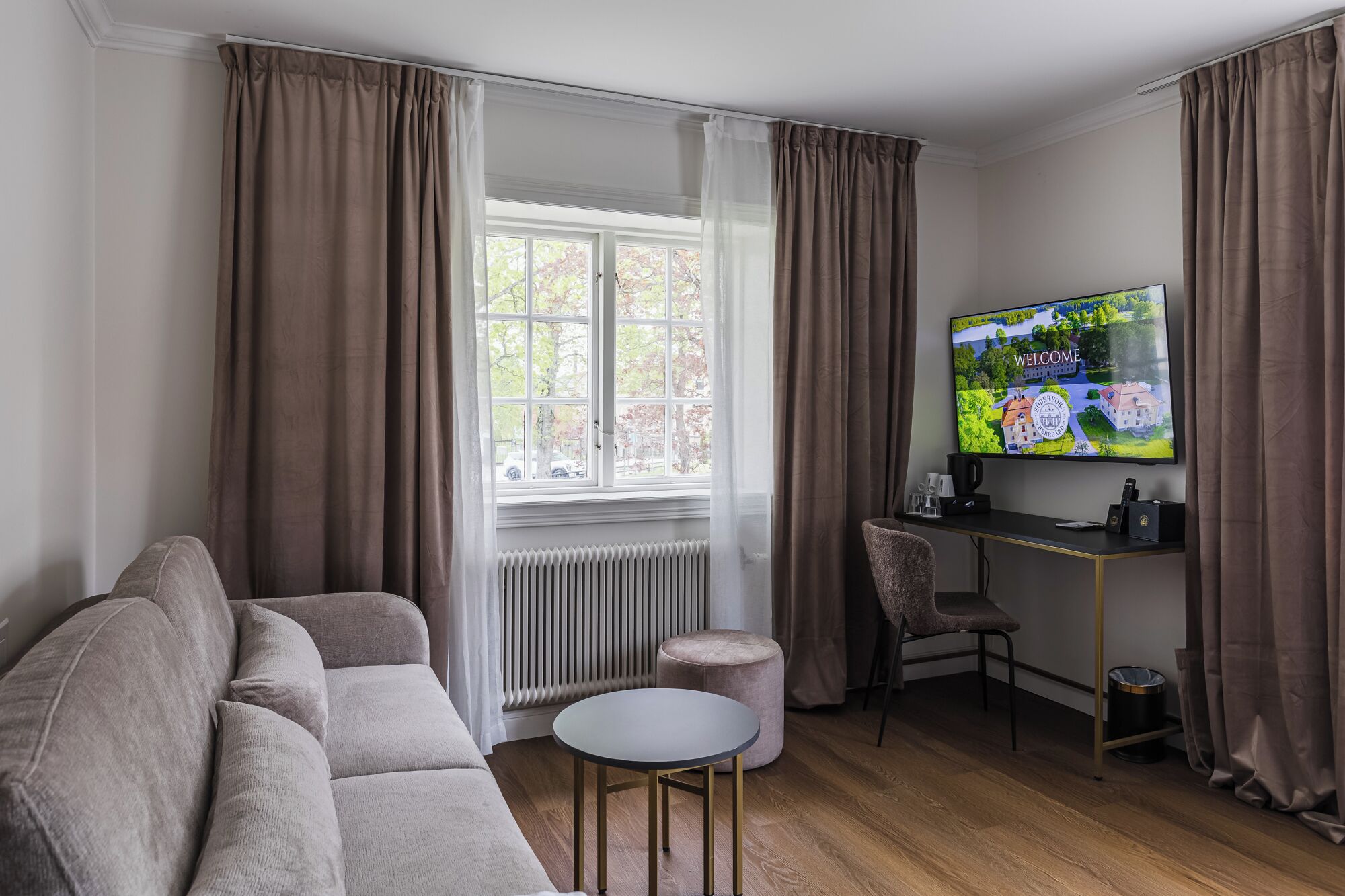 A living room with a sofa, a round table, a TV, and a radiator.