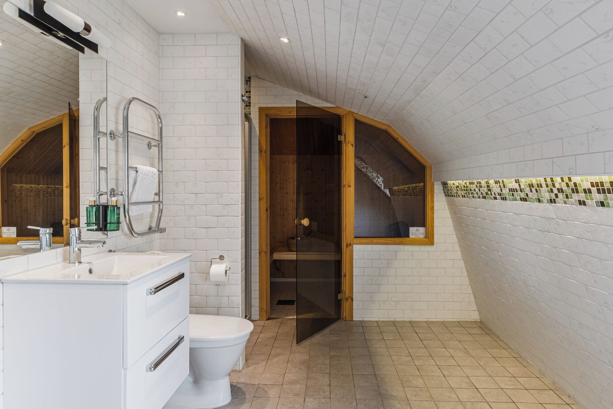 Une salle de bain moderne avec un mur recouvert de carreaux blancs, une porte en bois donnant accès à la douche, et un meuble-lavabo blanc avec un miroir.