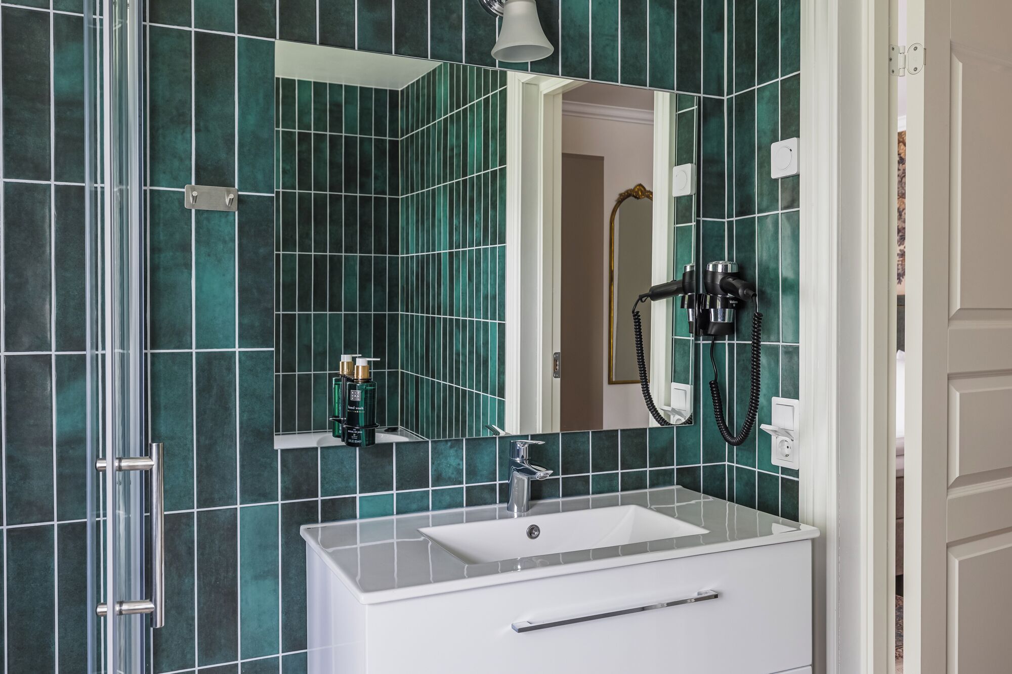 Een badkamer met een wit wastafel, een spiegel en een haardroger bevestigd aan de muur.