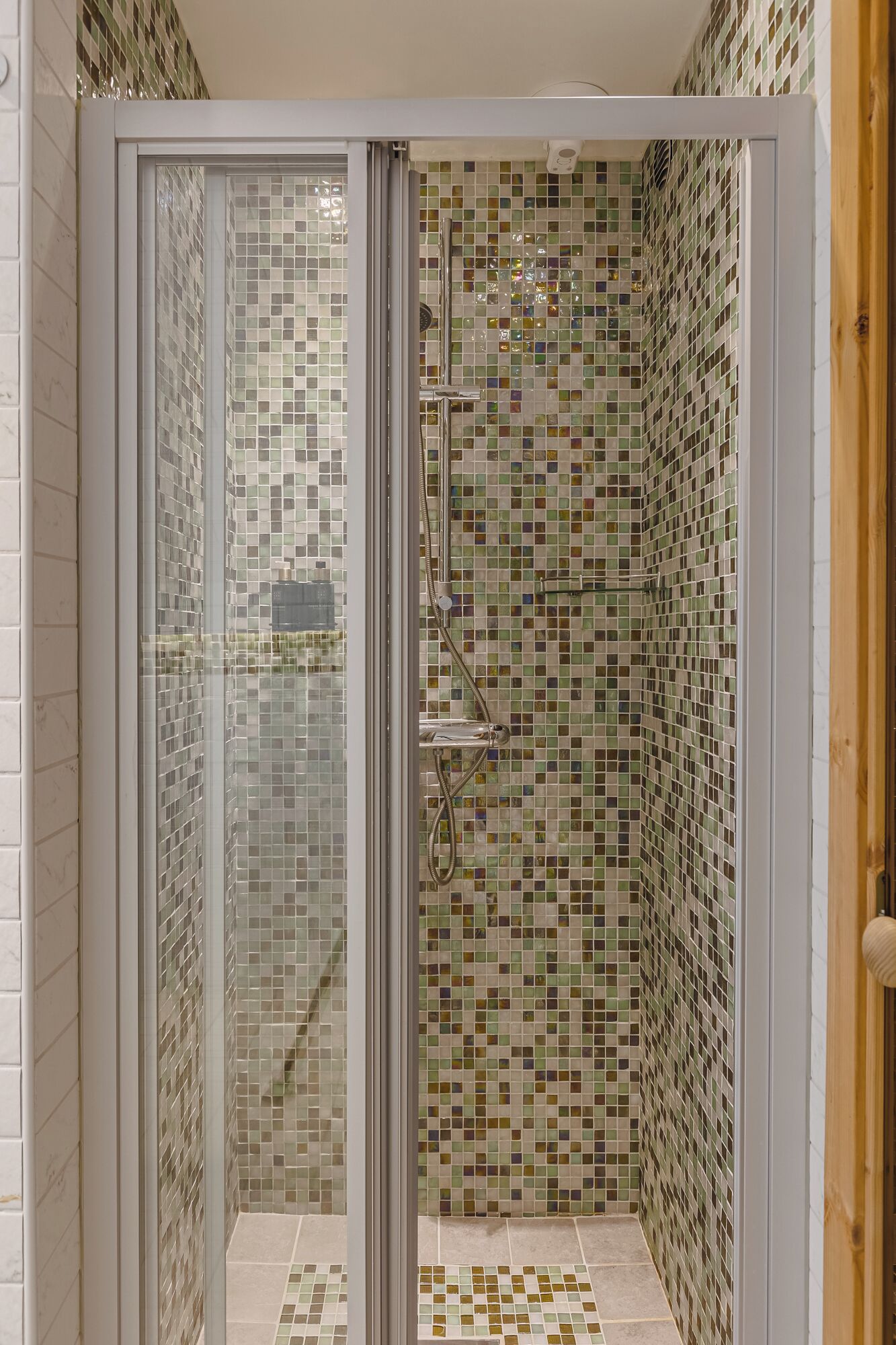 Una ducha con puerta de vidrio, paredes con azulejos y un cabezal de ducha.