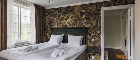 Un dormitorio con una cama grande, una araña, una pared con un diseño de árbol y una puerta que da a otra habitación.