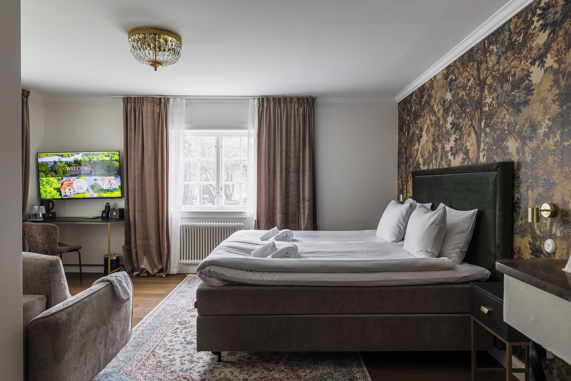 Una habitación de hotel con una cama, un escritorio con computadora, televisión y una ventana con cortinas.