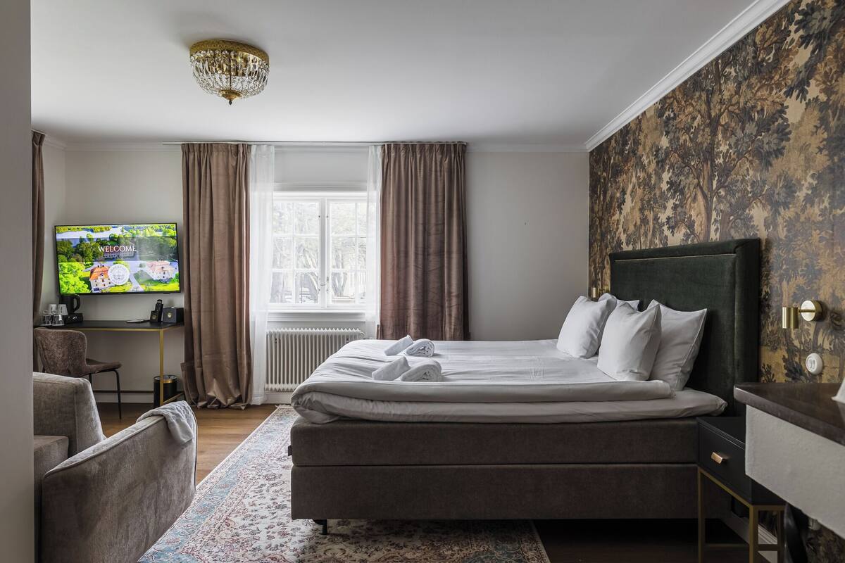 Una habitación de hotel con una cama, un escritorio con computadora, televisión y una ventana con cortinas.