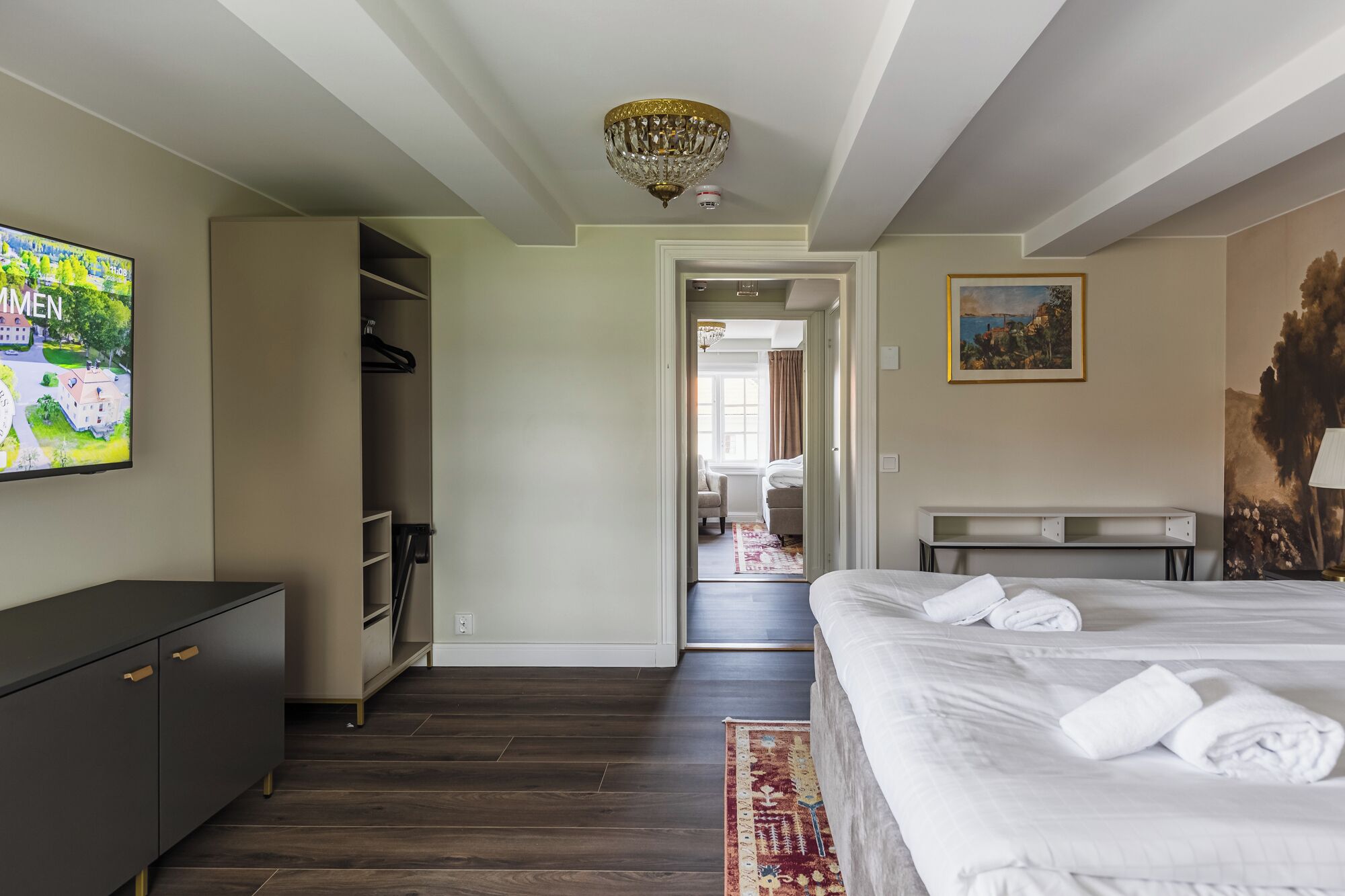 A hotel room with a bed, a desk, a wardrobe, and a TV displaying a landscape.